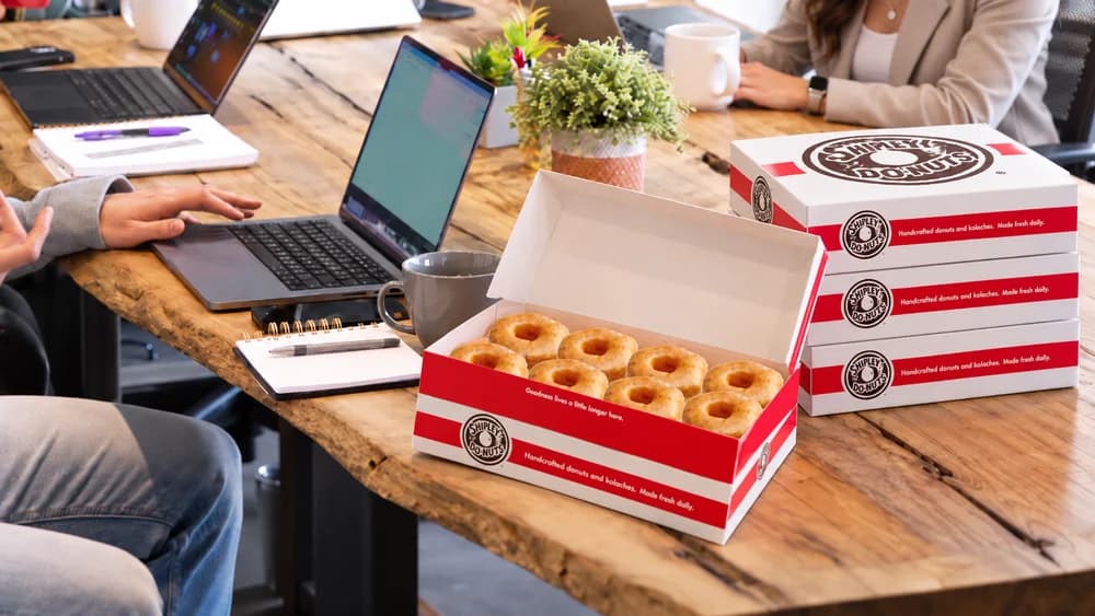 An open box of Shipley donuts shared around an office table